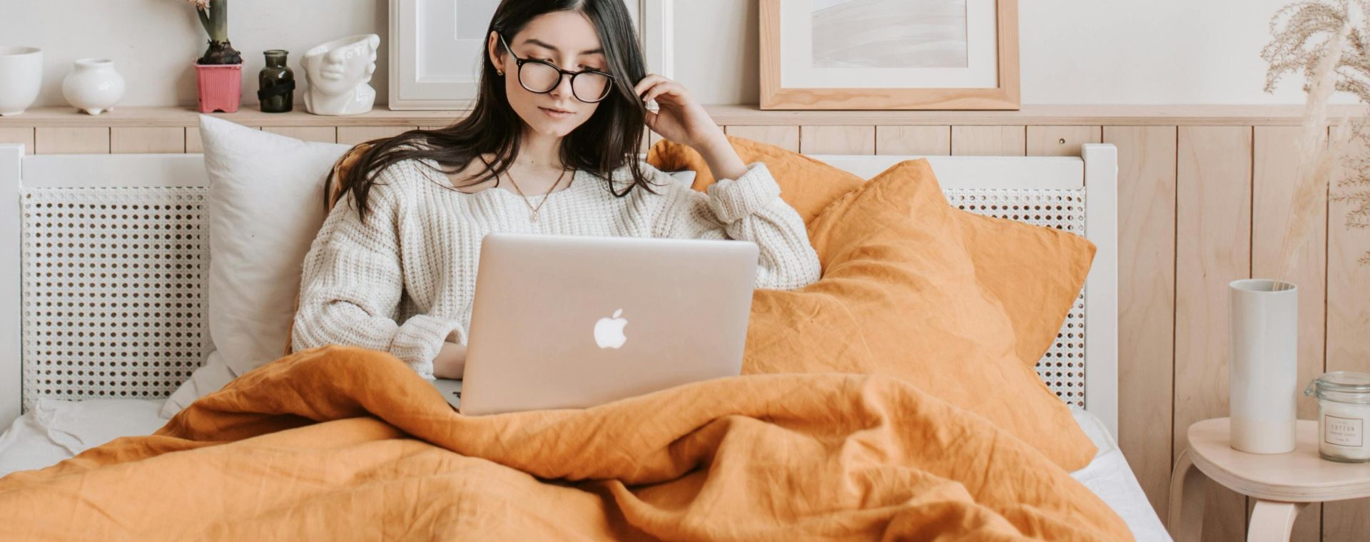 Young woman in cozy bedroom using a laptop, surrounded by stylish decor and art.