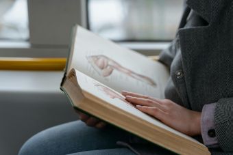 Close-up of hands holding an anatomy book, studying human muscles in a train.