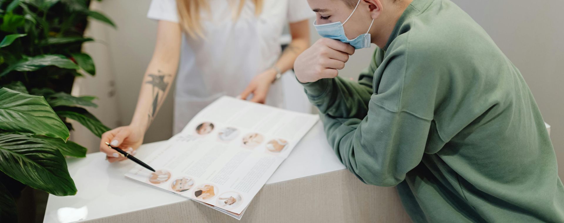 A healthcare professional and young man engaged in a consultation at a clinic, both wearing face masks for safety.
