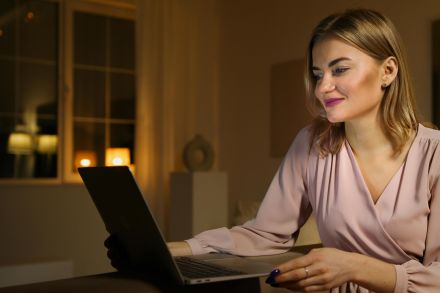 A woman browsing the internet on a laptop in a cozy indoor setting during the evening.